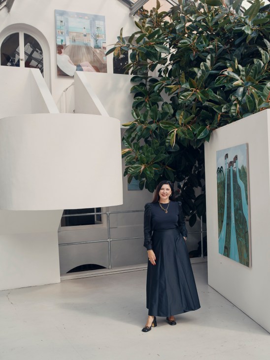 Kristin Hjellegjerde stands in her gallery space surrounded by white architectural elements and large potted plants.