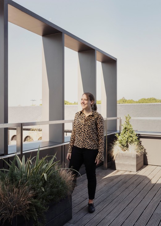 Woman in leopard print shirt standing on wooden deck beside planters overlooking waterfront.