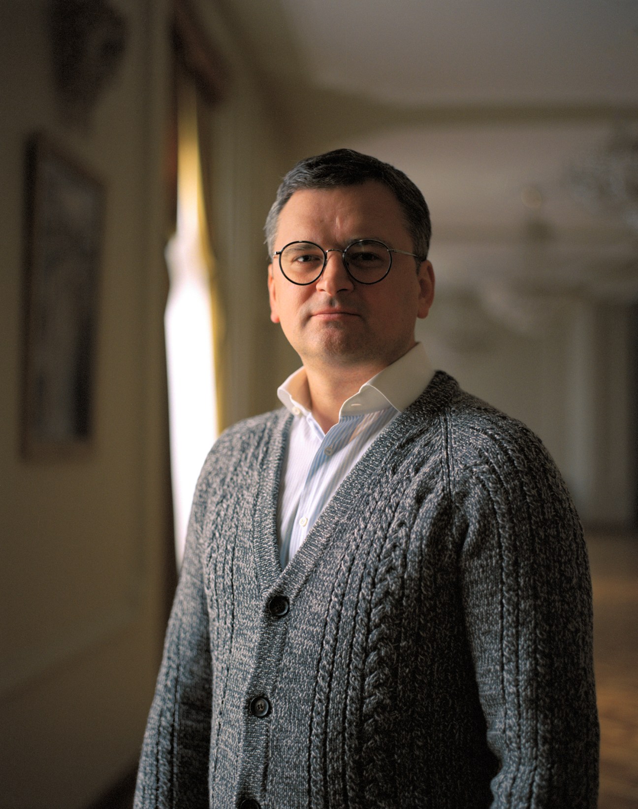 Dmytro Kuleba wearing glasses and a grey cardigan over a white shirt, sitting in his office