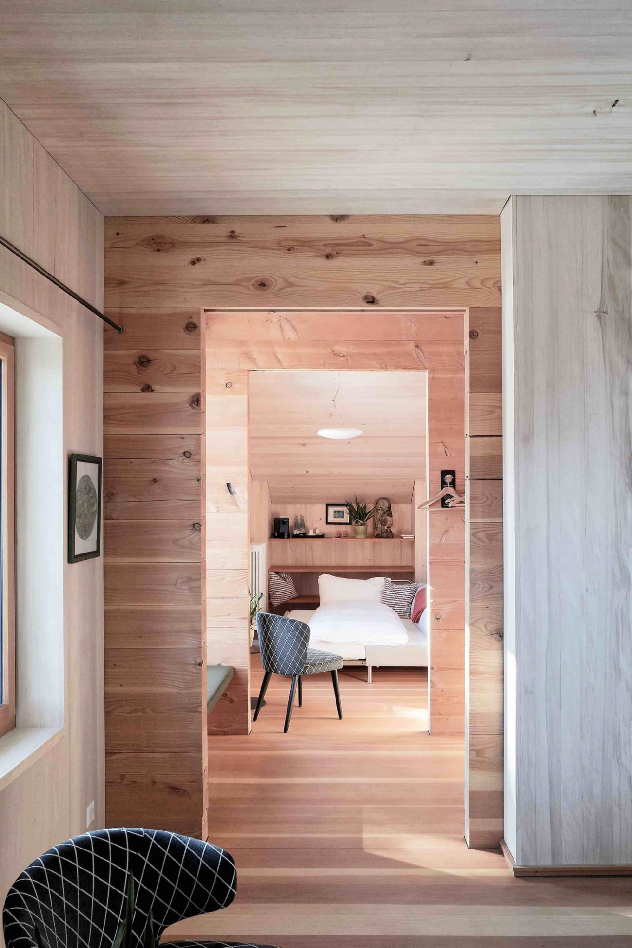 Cozy hotel room with wooden walls, built-in bed, shelving, chair, and mountain view through window