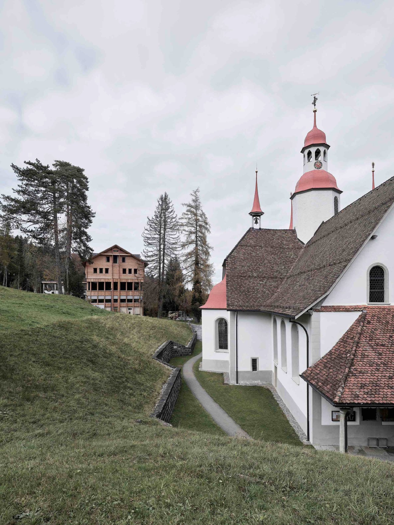 Historic white church with red onion dome and bell tower nestled among evergreen trees in mountain setting