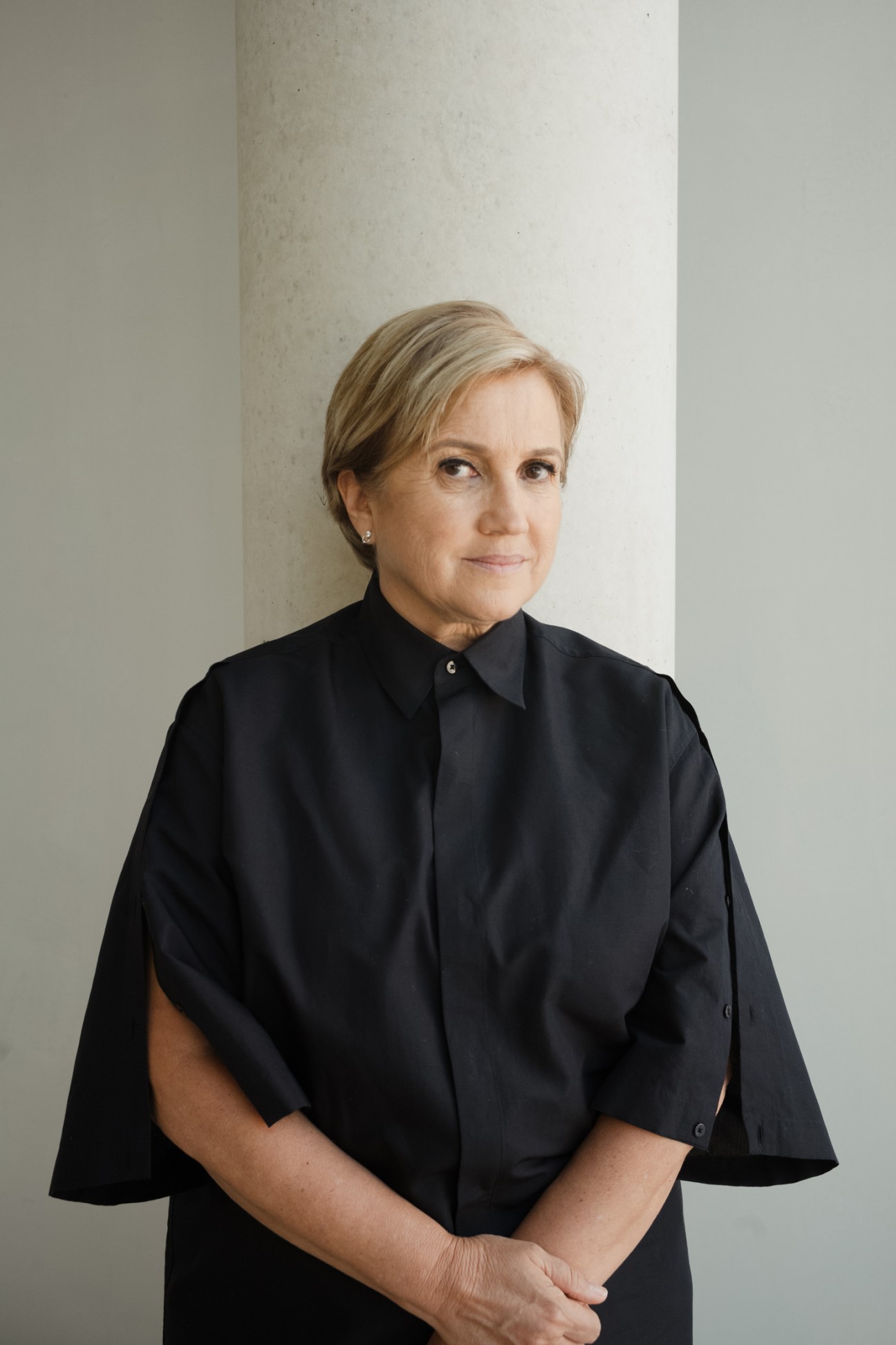 Silvia Venturini Fendi poses in a black cape-style shirt against a neutral stone column background