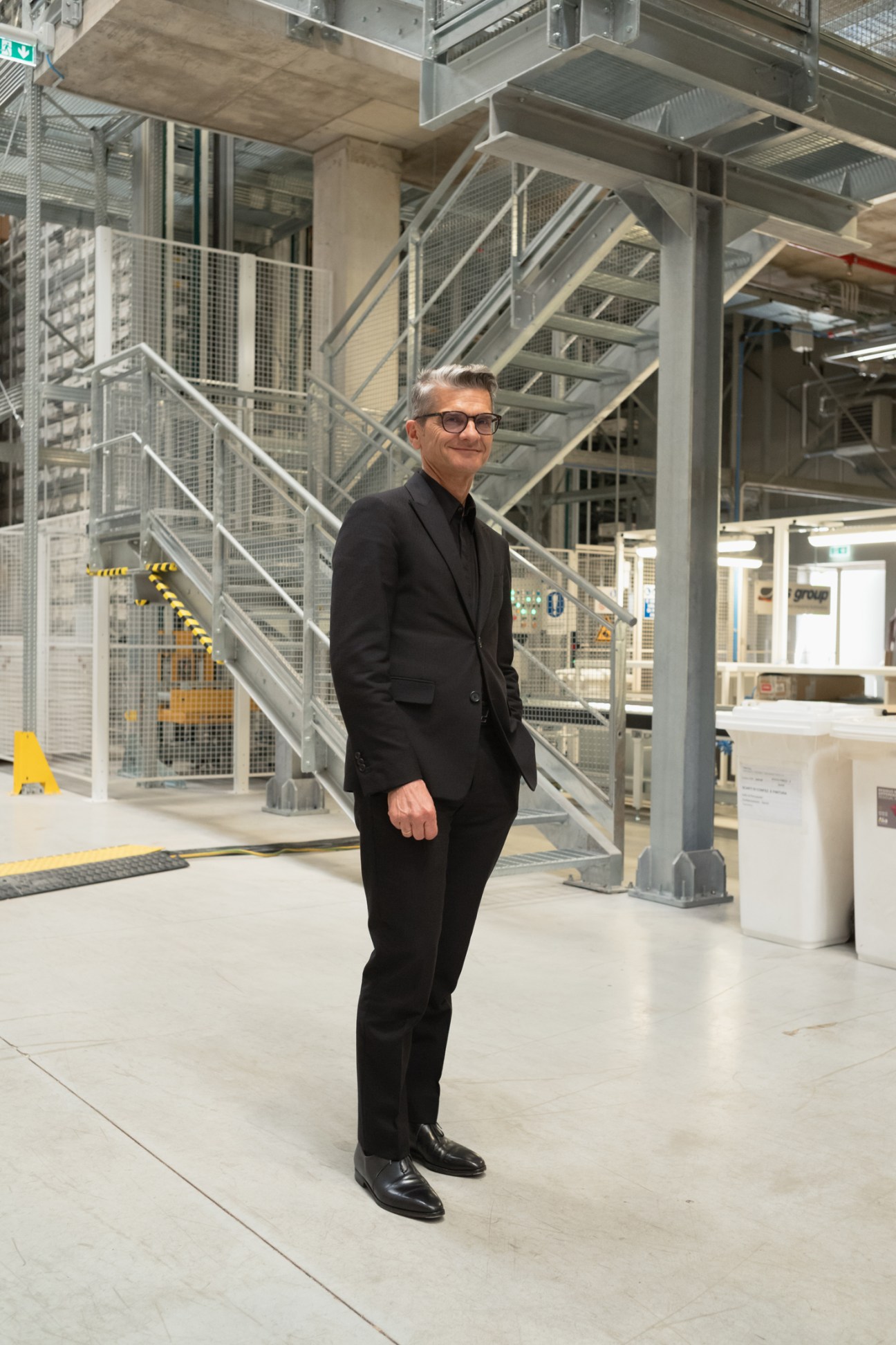Serge Brunschwig in a black suit standing in Fendi's modern Roman headquarters with metal stairs and industrial design