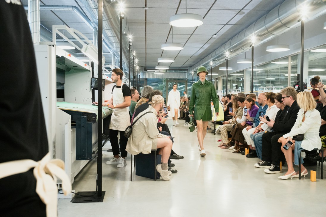 Models walk down a fashion runway set up in Fendi's factory workspace with seated audience watching the show
