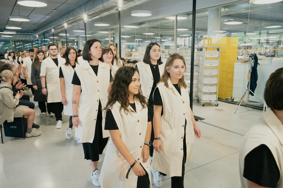 Group of Fendi artisans in white lab coats walking together through modern workshop facility with glass walls