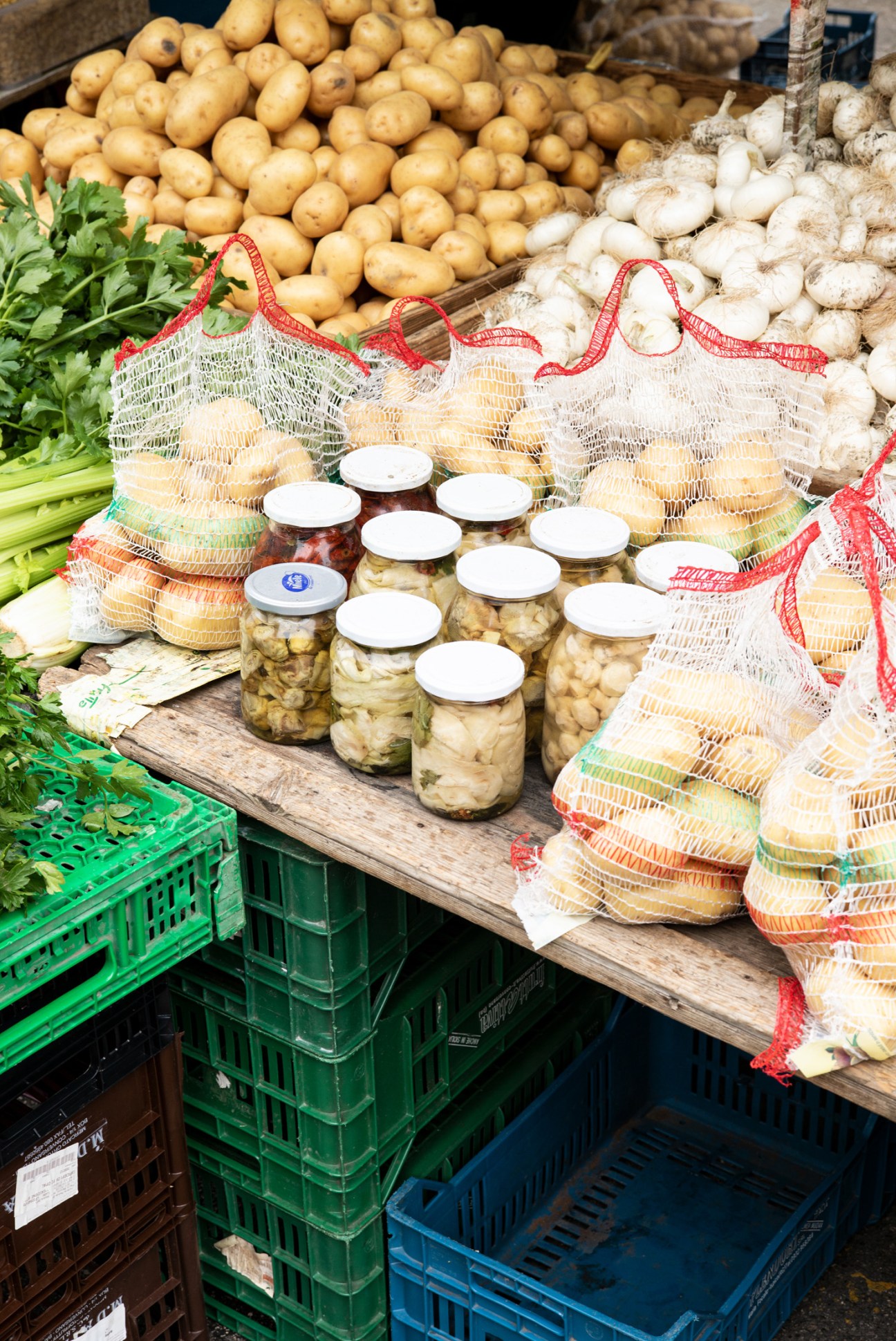 Market produce display with potatoes, mushrooms, jarred goods, fresh herbs and mesh bags in Bari.