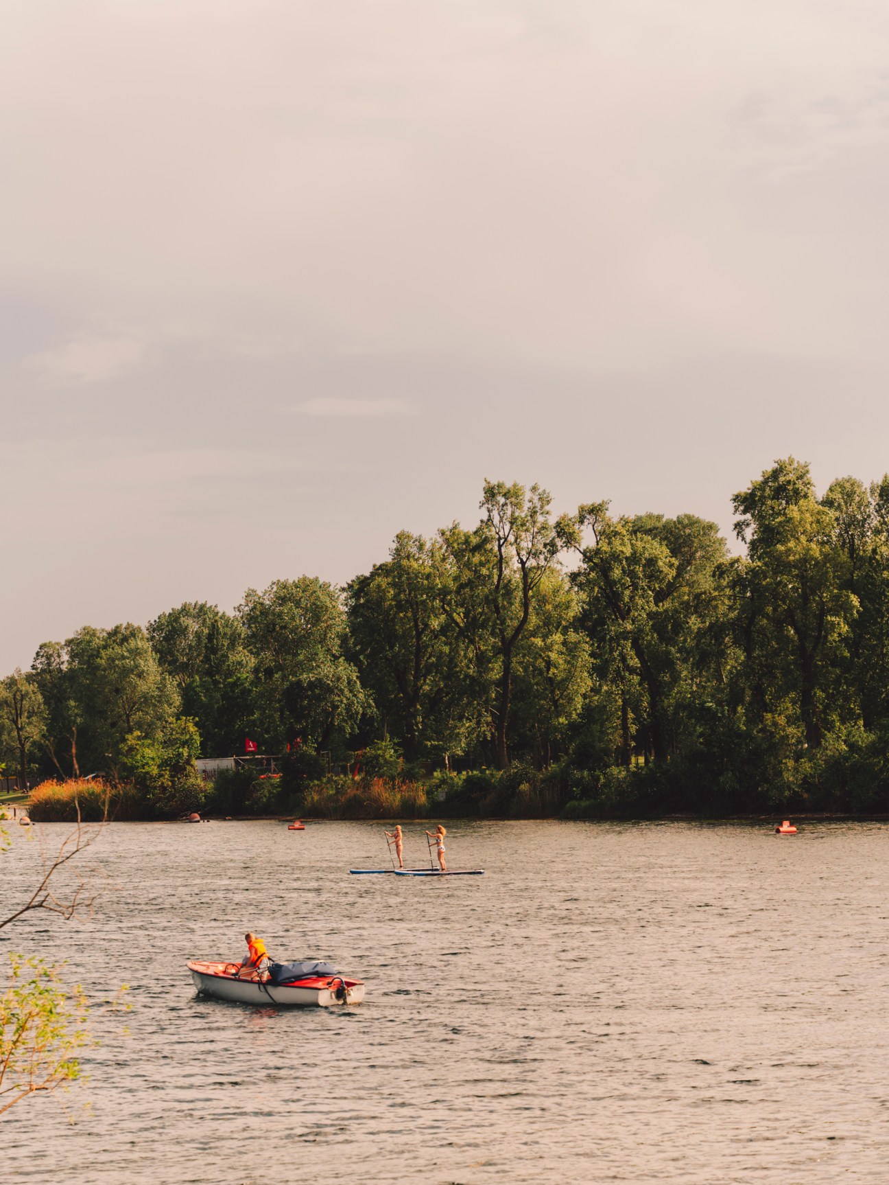 Person in small boat on lake with trees lining the shore under overcast sky