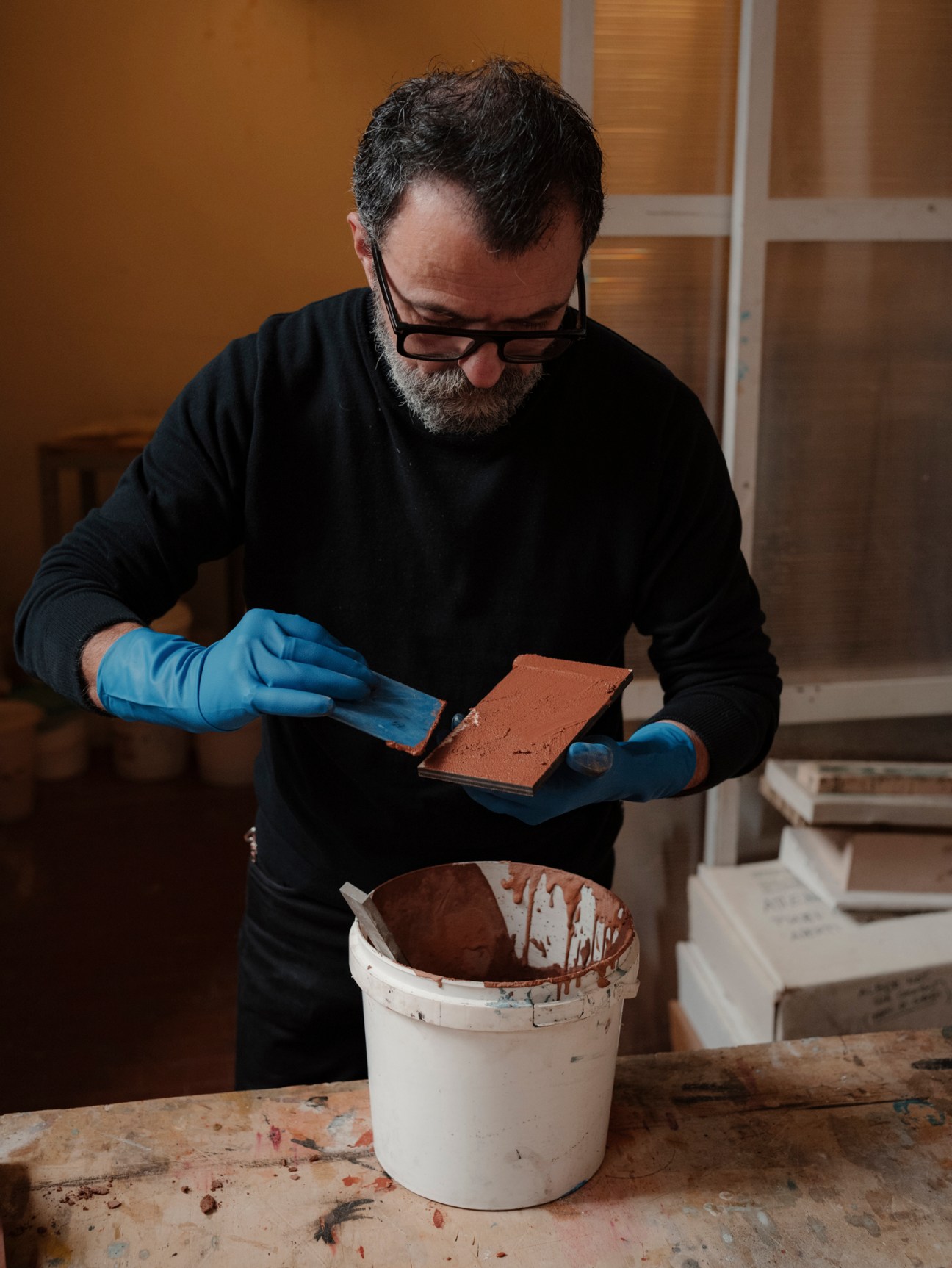 Marco Galofaro in blue gloves applying material to an architectural model in his Rome workshop