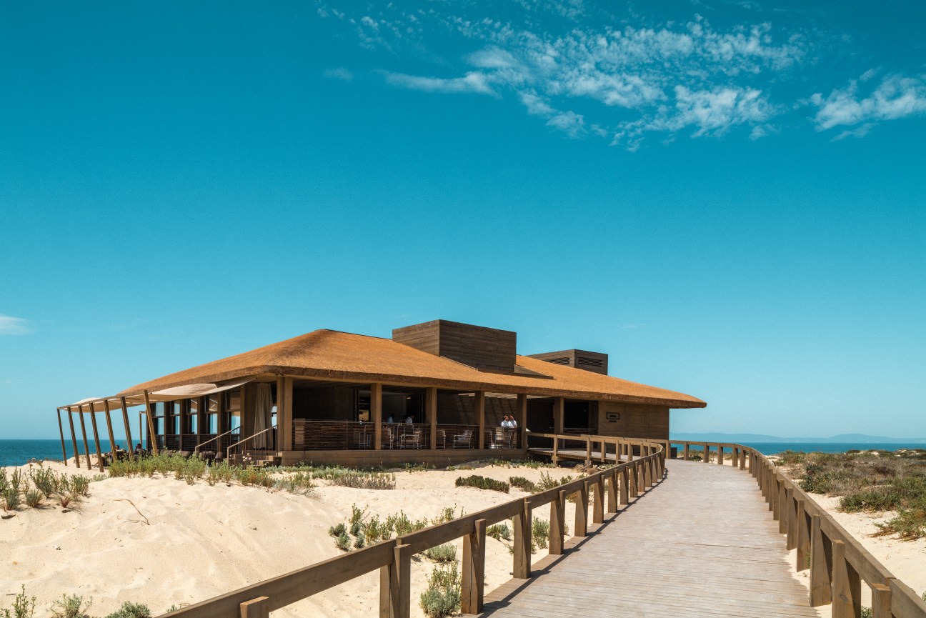 JNcQUOI Beach Club exterior with thatched roof and ocean view