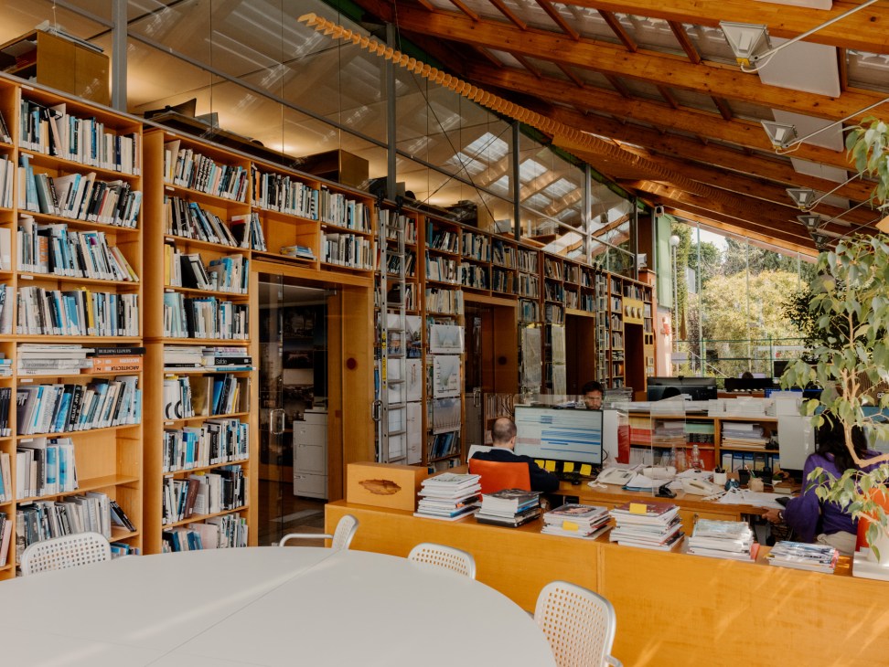 Interior view of bright studio space with large windows, work tables and architectural models scattered throughout