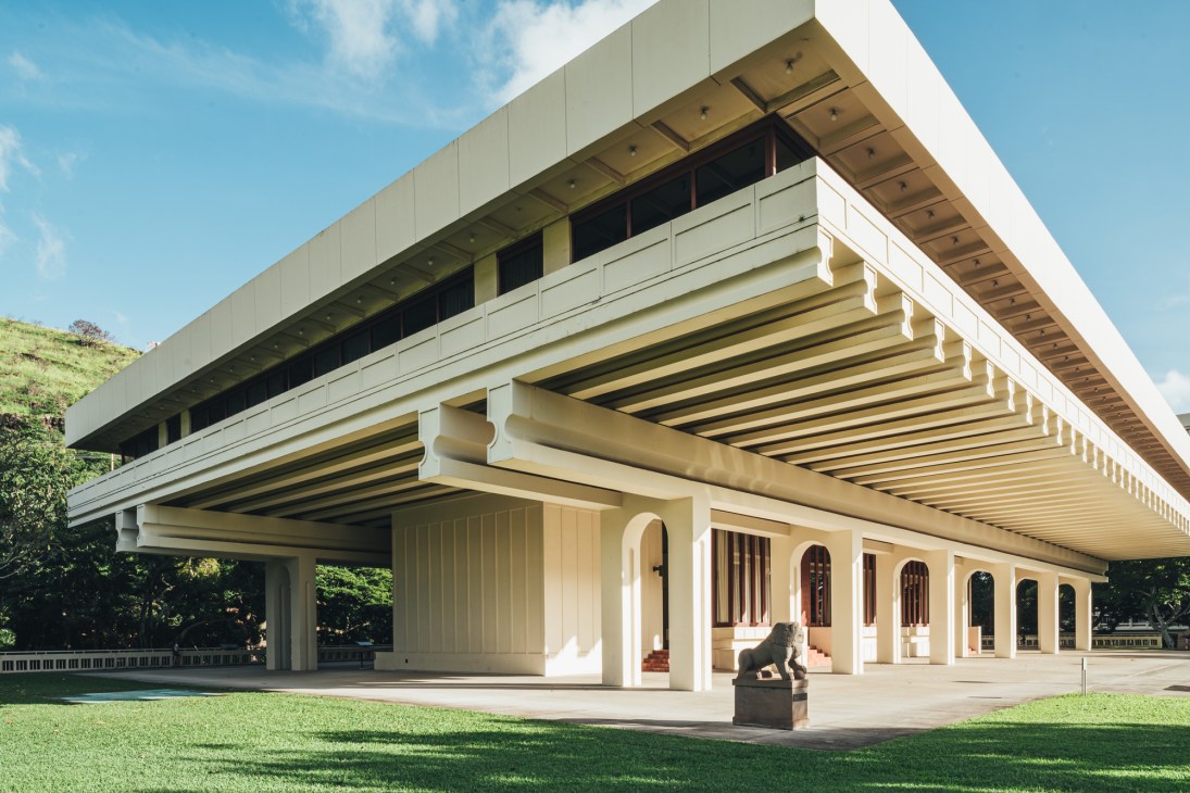 Modernist university building elevated on pillars creating shaded outdoor space underneath with students gathering below