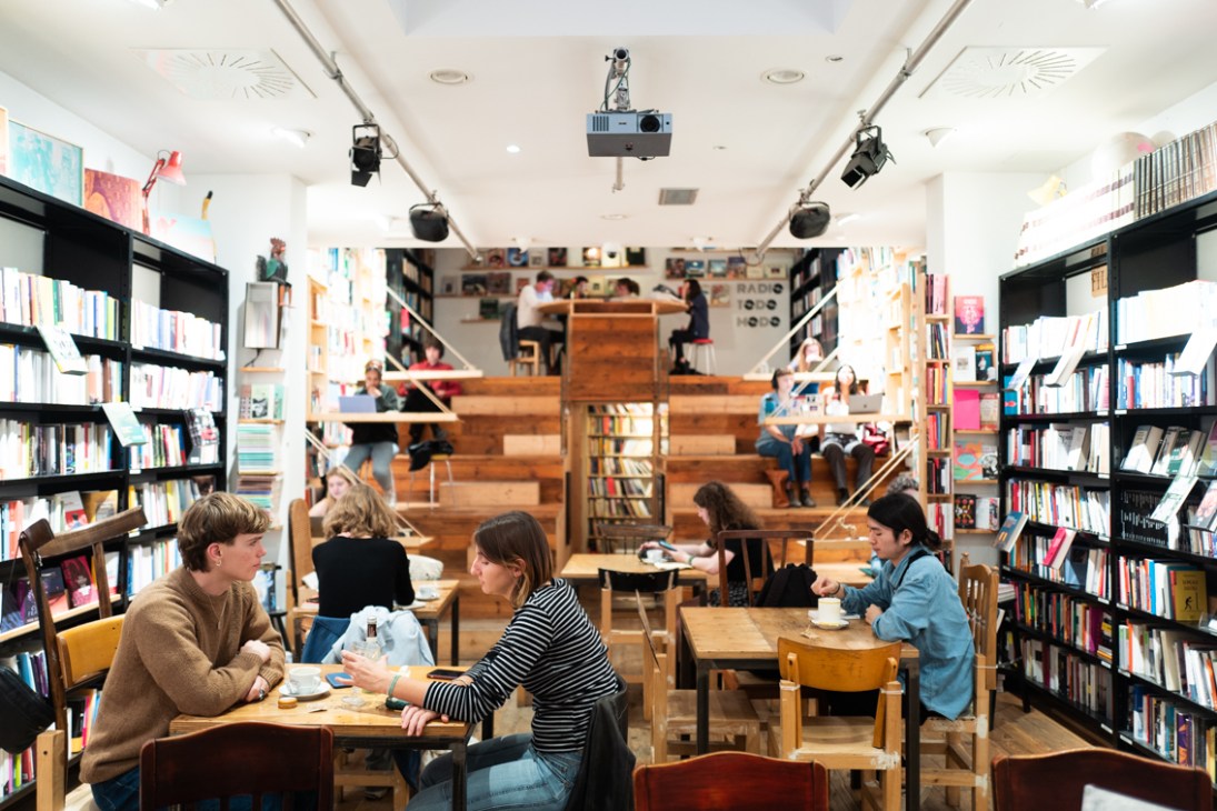 Modern bookstore interior with wooden tiered seating, black bookshelves, and customers reading at tables