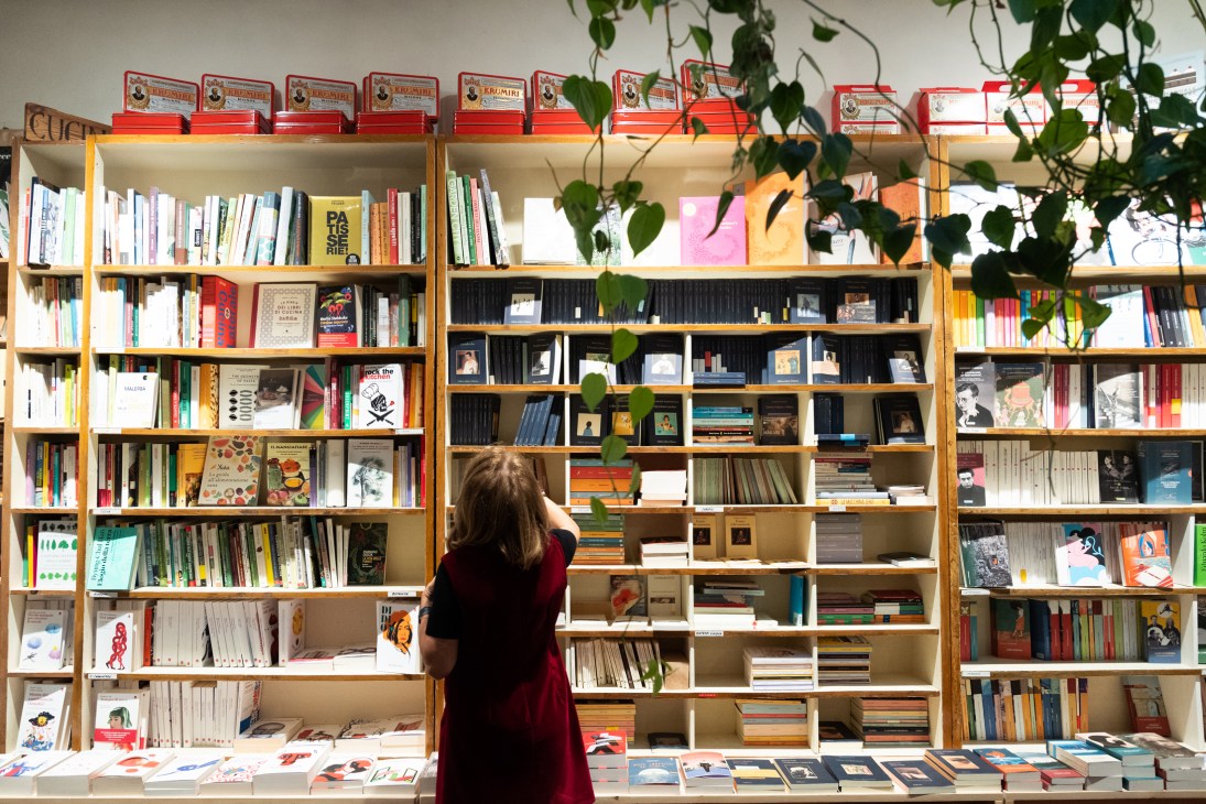 Floor-to-ceiling wooden bookshelves filled with books and a person in red browsing