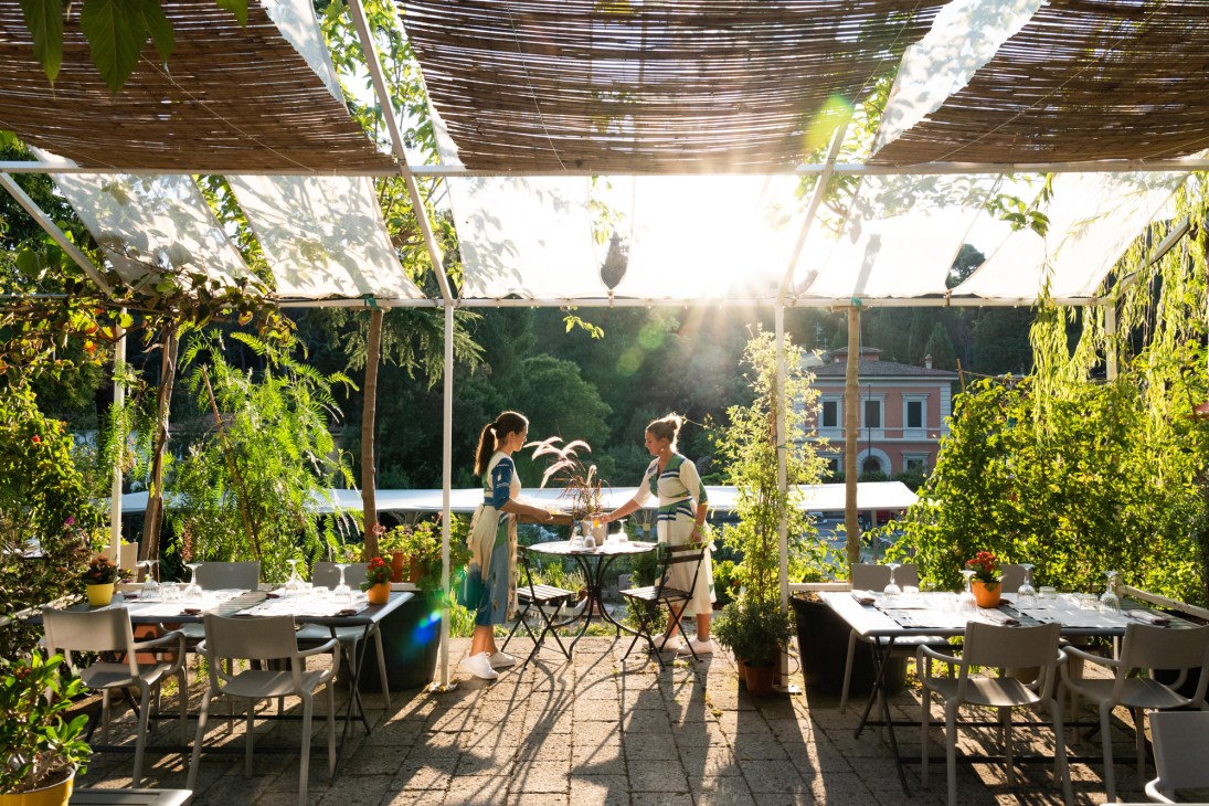 Two people dining at outdoor table under pergola surrounded by lush greenery at Le Lune restaurant in Florence