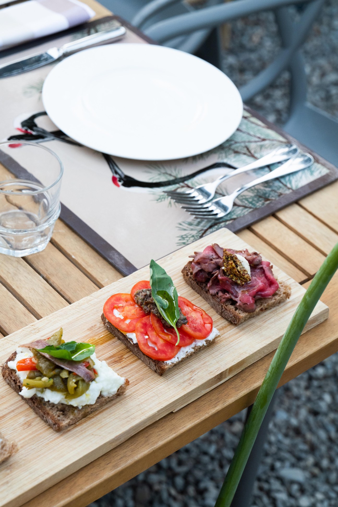 Artisanal open-faced sandwiches on dark bread with tomatoes, cured meat, and pickled vegetables on wooden serving board