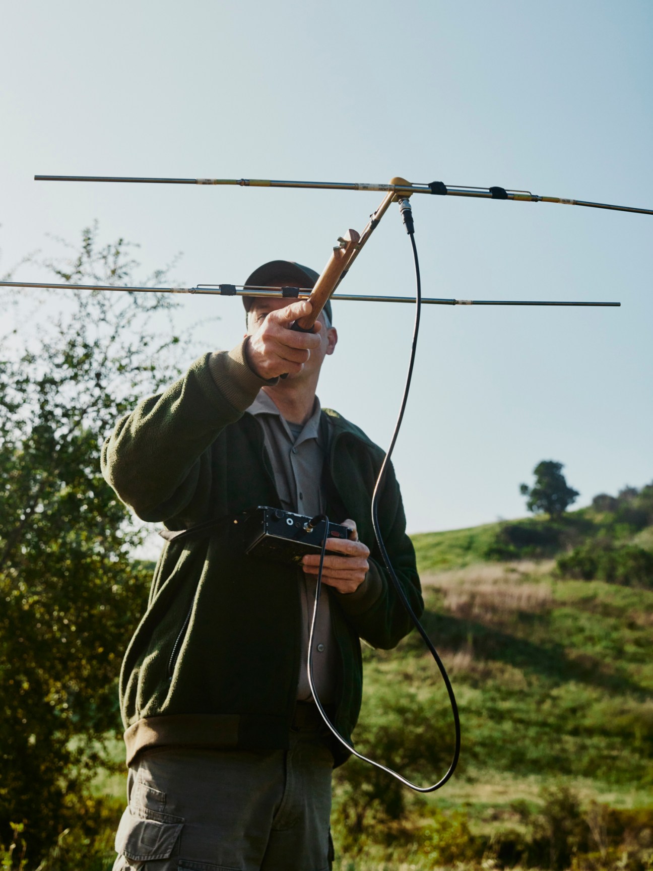 Person in dark clothing using directional antenna equipment to track wildlife in outdoor field setting