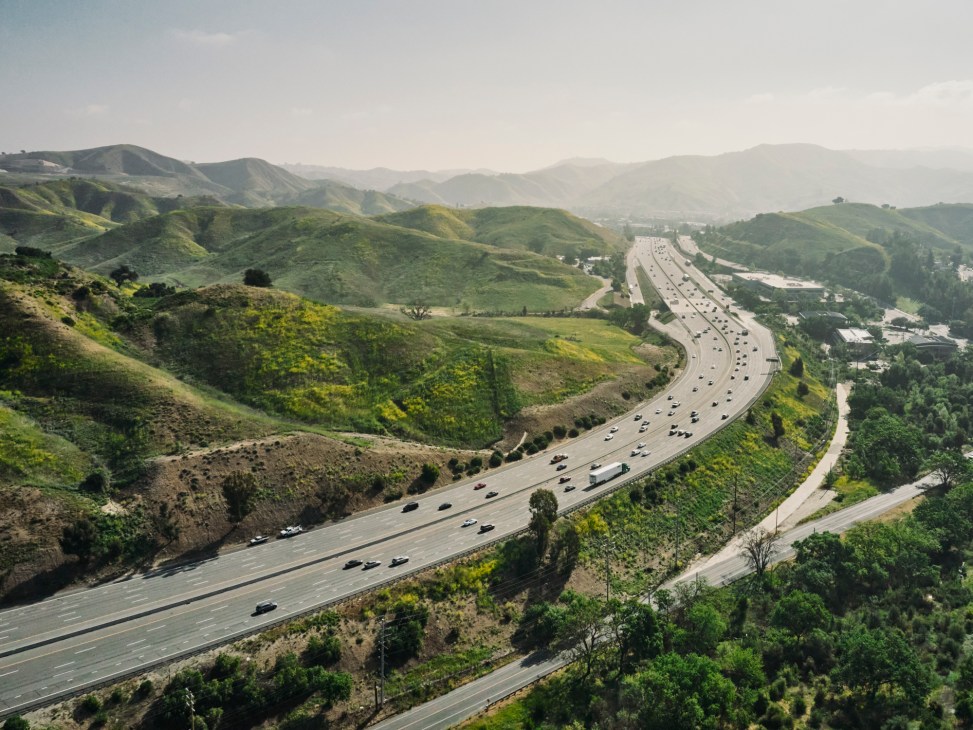 Aerial view of multi-lane freeway winding through green rolling hills and mountains