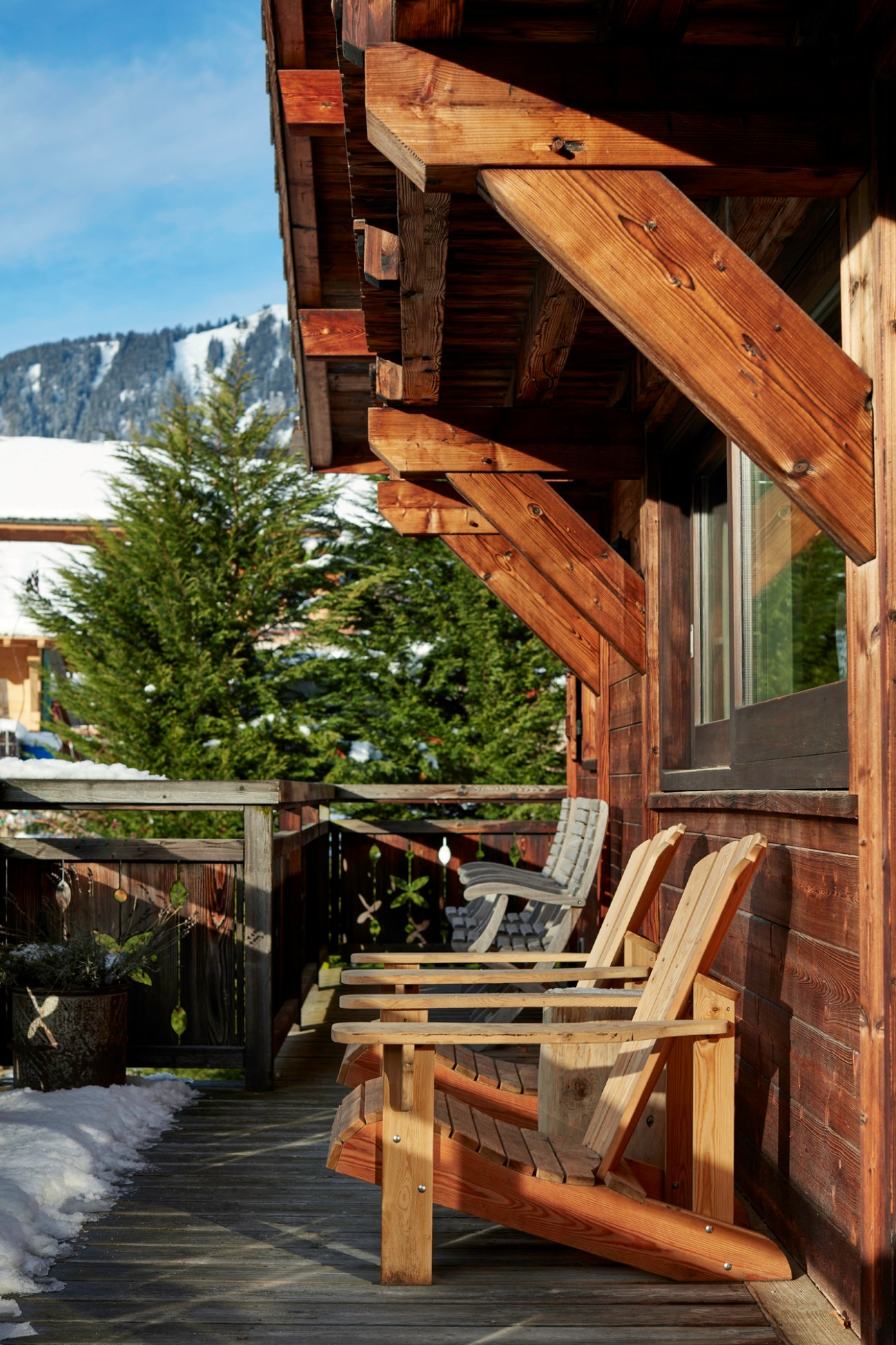 Wooden Adirondack chairs on a covered terrace of an Alpine chalet with snow-capped mountains in background