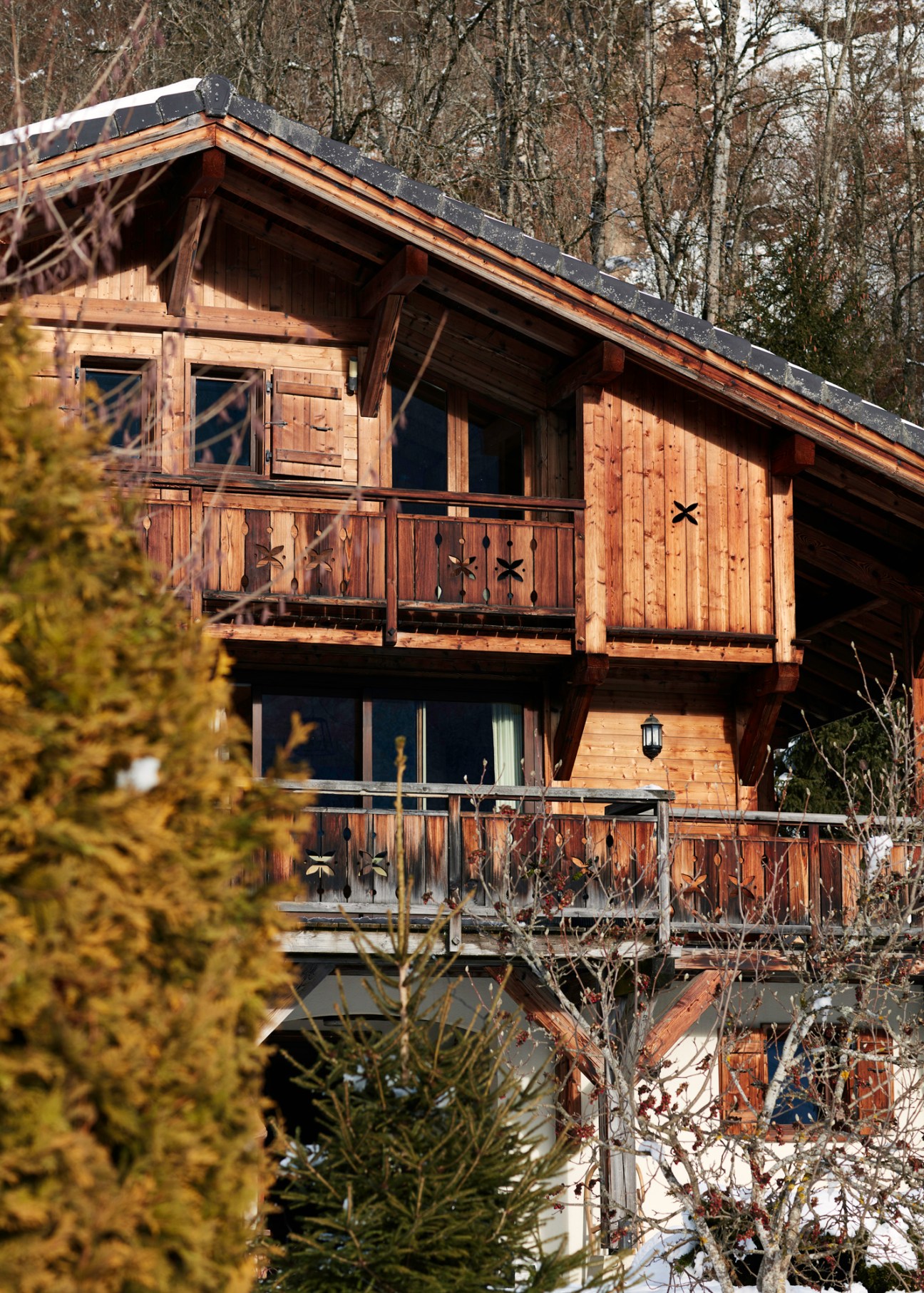 Traditional wooden chalet with balconies and snow-covered roof nestled among bare winter trees