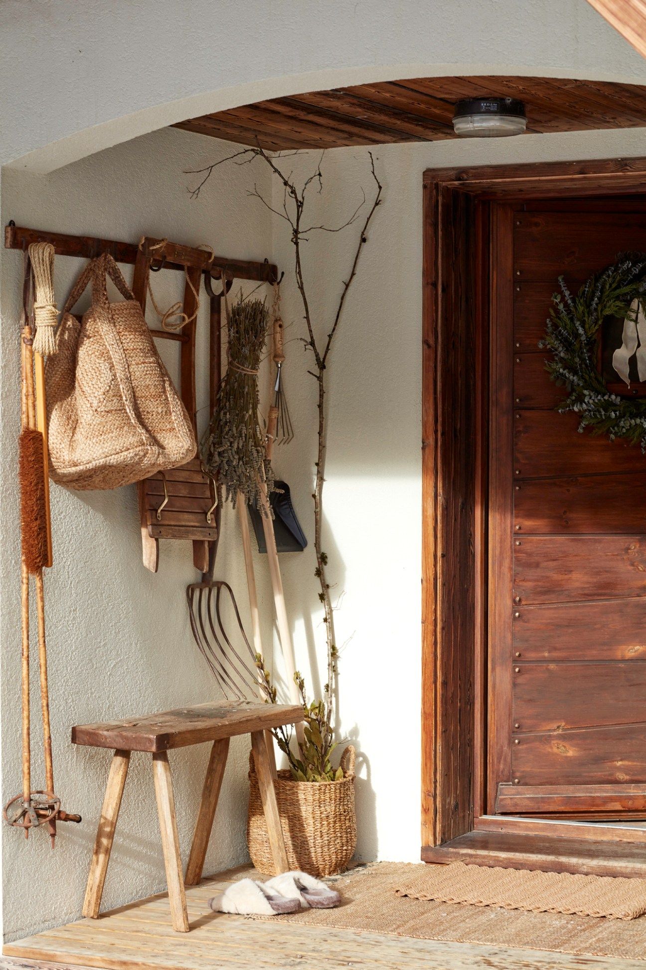 Rustic entryway with woven bags, wooden bench, dried herbs and natural materials hanging from wooden beam