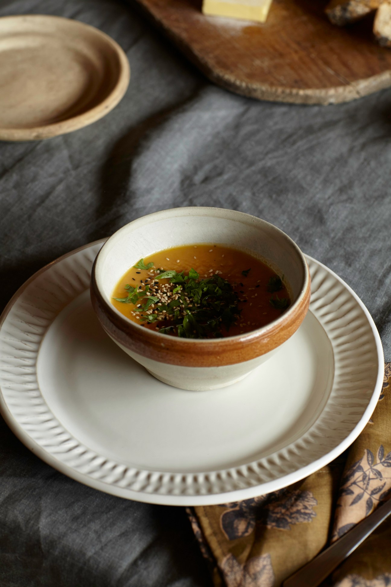 Bowl of soup with herbs and sesame seeds served in ceramic bowl on ridged plate