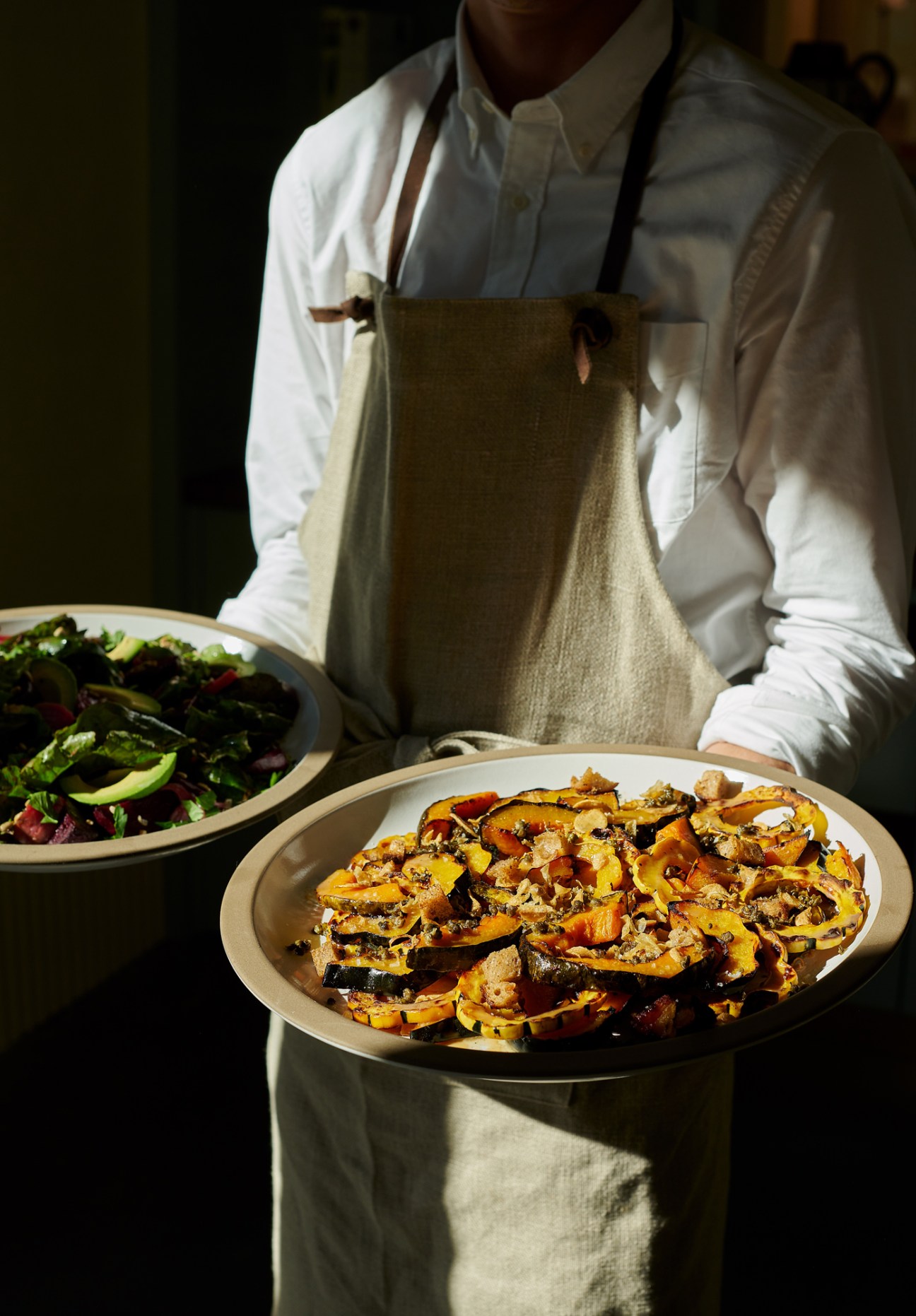 Server in apron carrying plates of roasted vegetables and salad at Le Bon Nosh