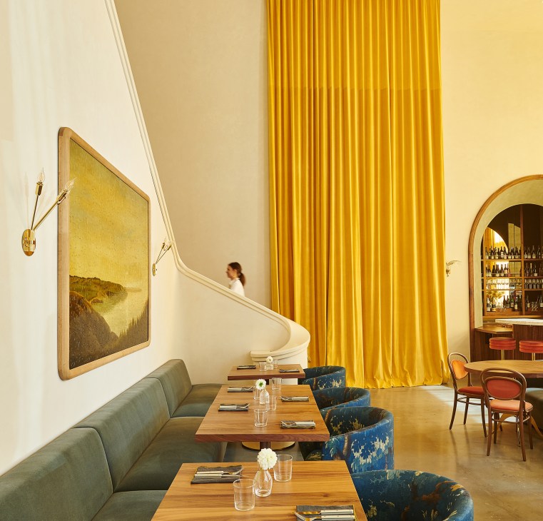 Restaurant interior with golden yellow curtains, curved staircase, and dining tables with banquette seating