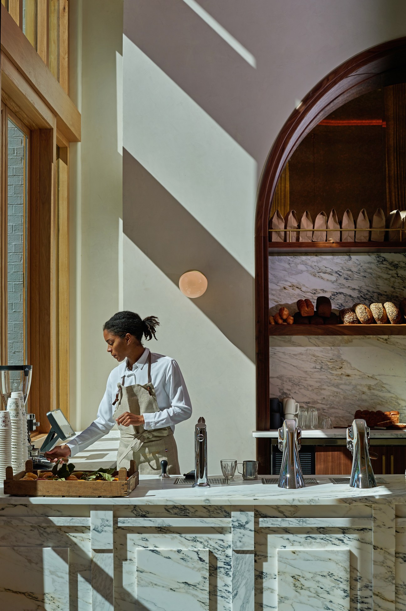 Professional chef in white shirt and apron working at marble kitchen island with bread shelves in arched alcove