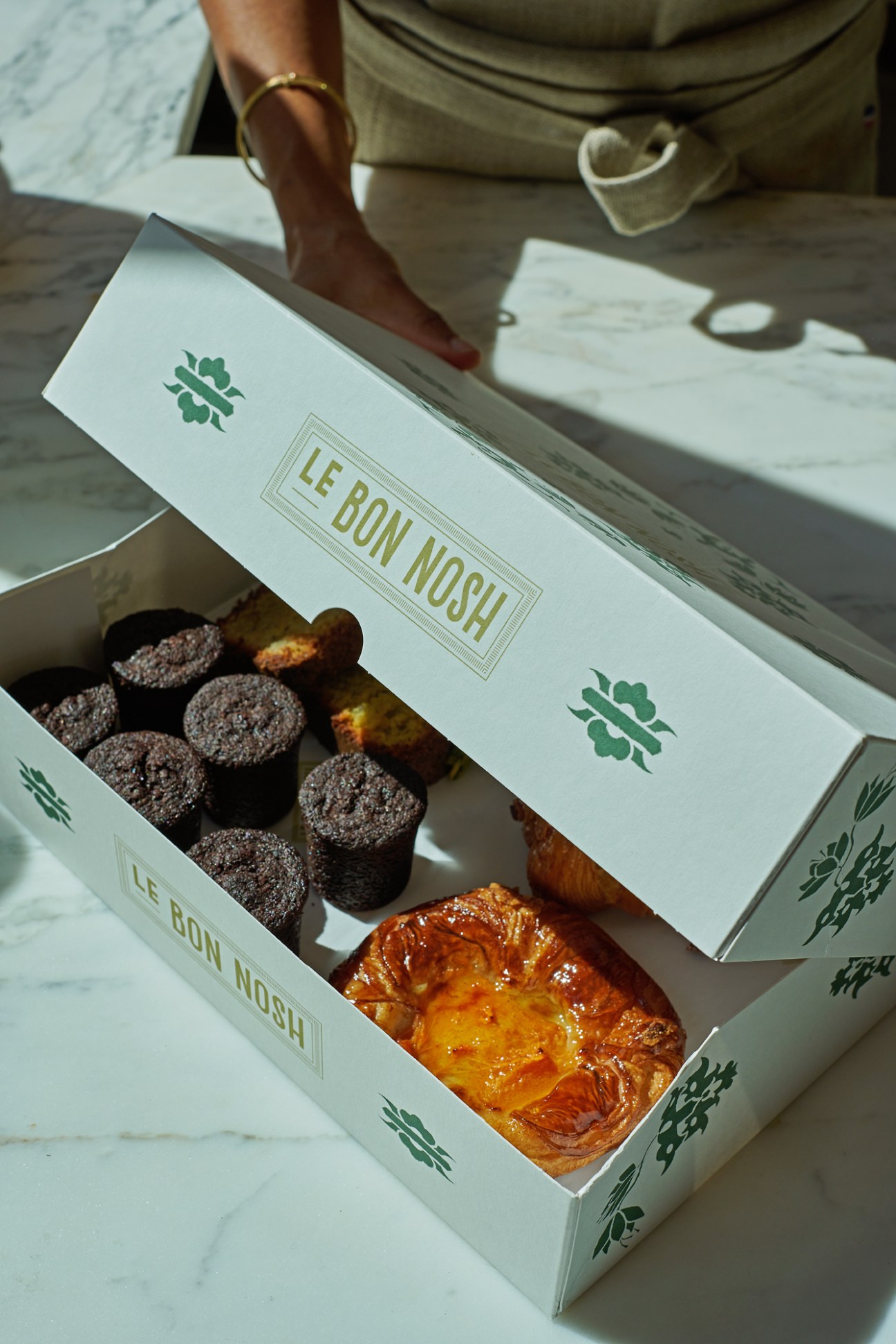 White boxes from Le Bon Nosh containing chocolate muffins and golden pastries