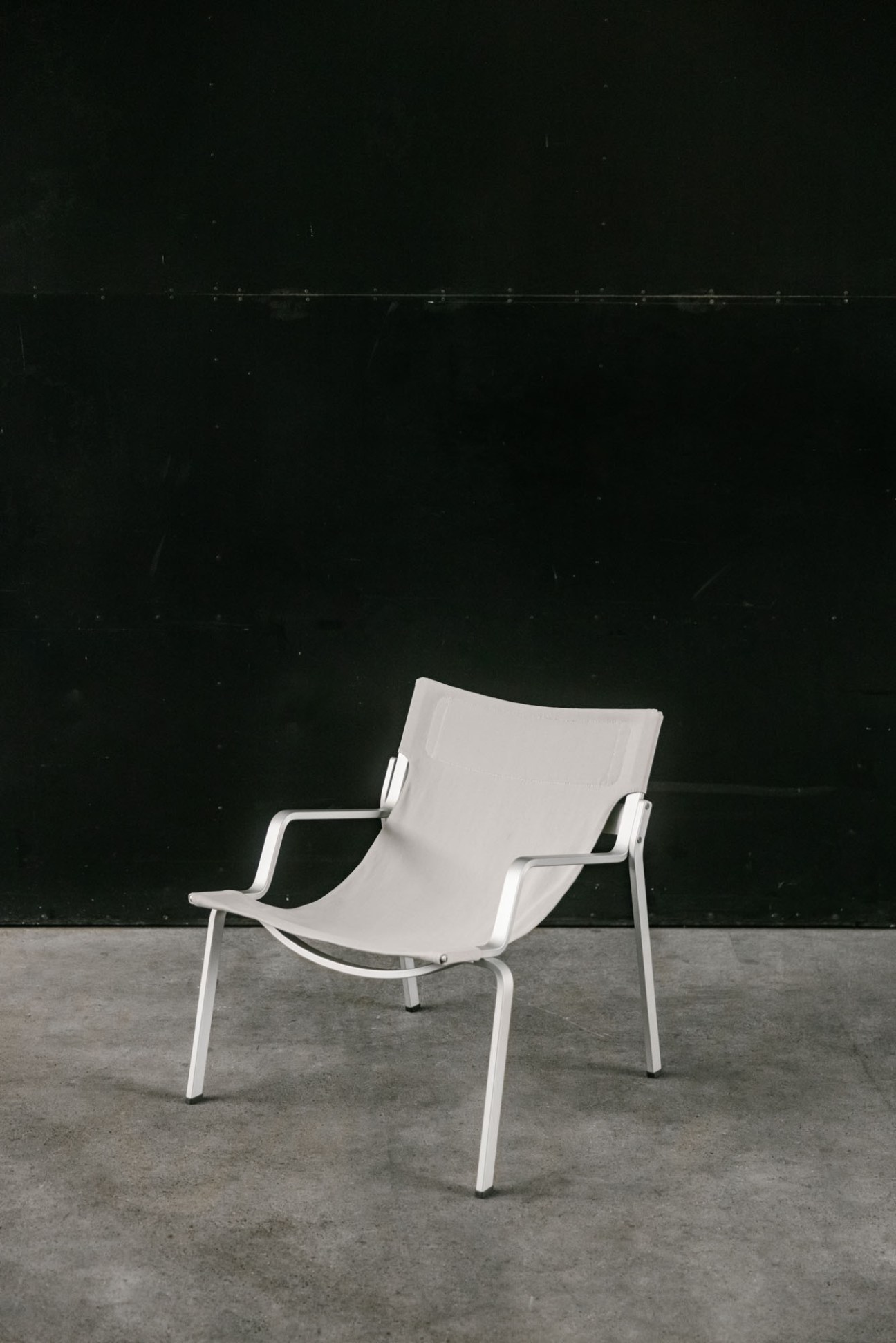 White aluminium chair with beige fabric seat cover against dark wall on concrete floor
