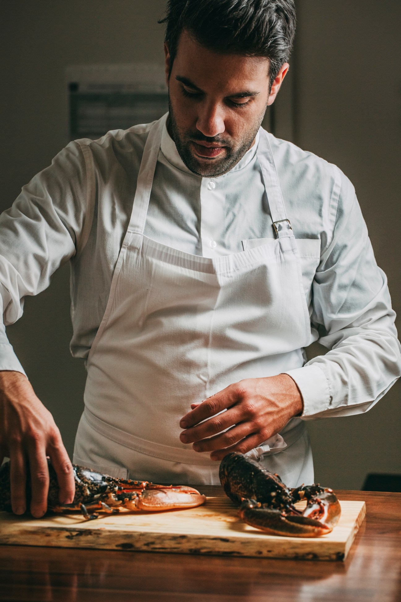 Chef in white apron preparing fresh lobsters on a wooden cutting board.