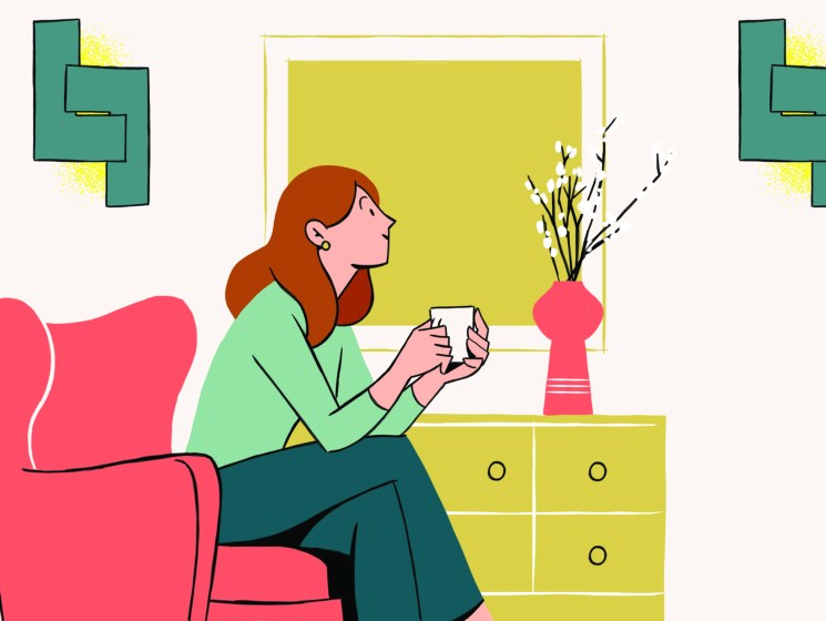Woman in green sweater sits in pink armchair holding coffee mug in bright, well-lit living room with yellow decor