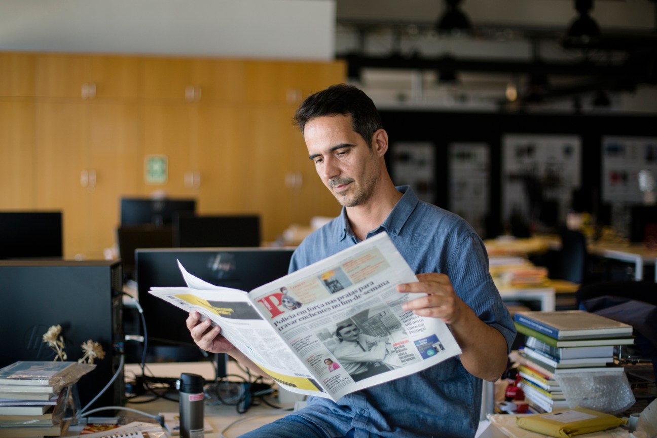 Tiago Luz Pedro, Público's editor-at-large, reads a newspaper in an office with a yellow wall.