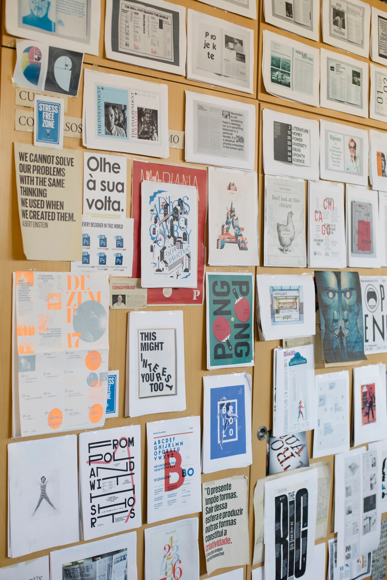 Collection of printed publications, posters, and design work pinned to a wooden board wall.