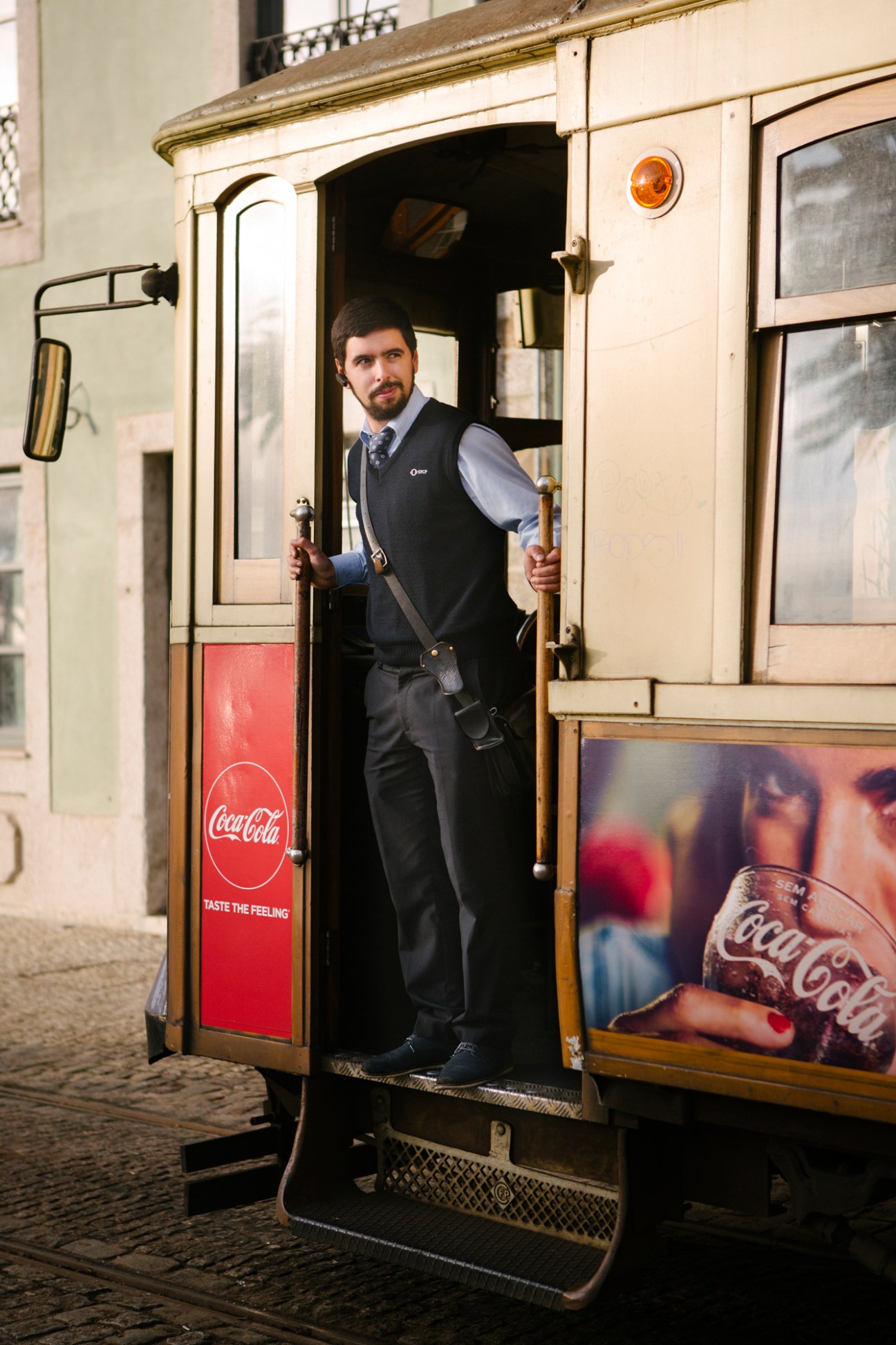 Man in business attire standing in doorway of vintage cream-colored tram with Coca-Cola advertisement.