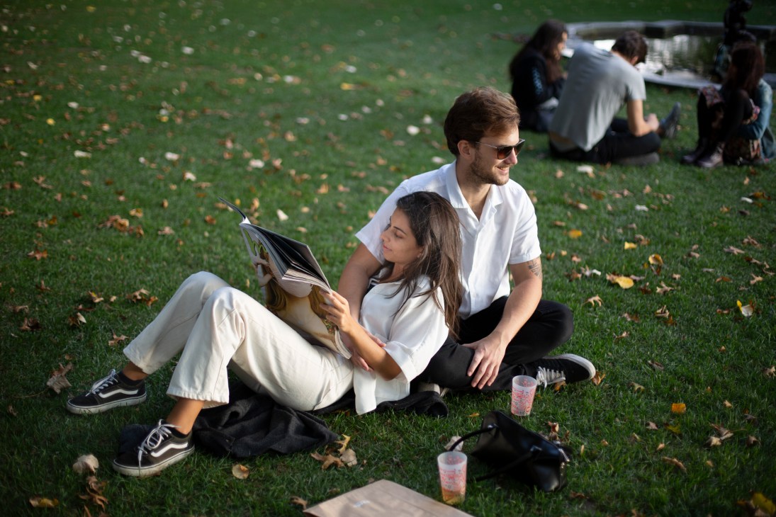 Couple reading magazine while sitting on grass in an urban park setting.
