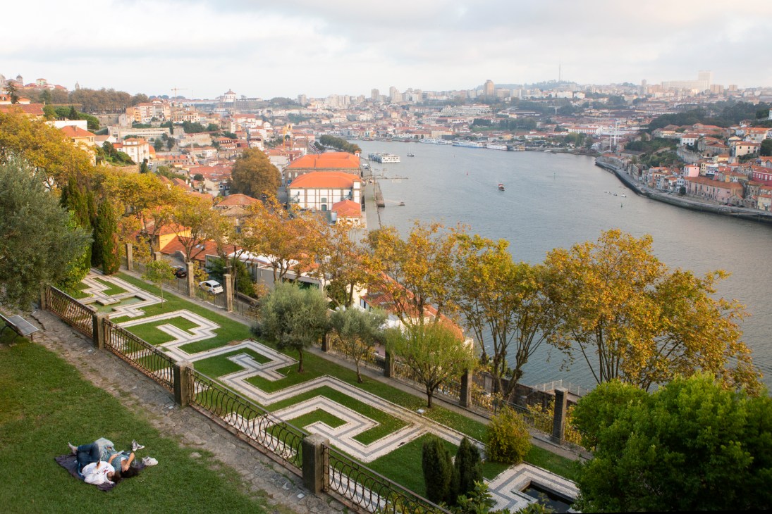 Terraced garden with geometric hedges overlooking Porto's riverside cityscape and orange-roofed buildings.