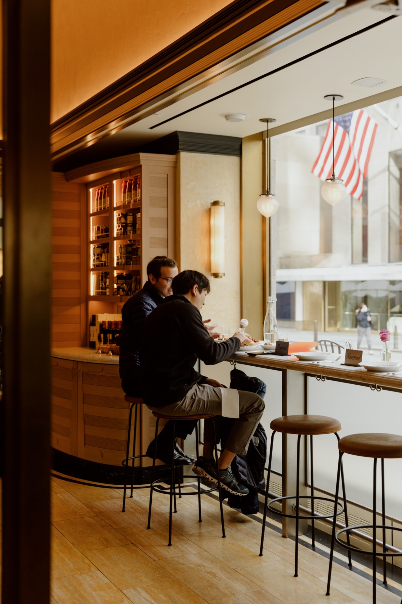 Two men sitting at a marble counter with bar stools in a restaurant with warm lighting and large windows