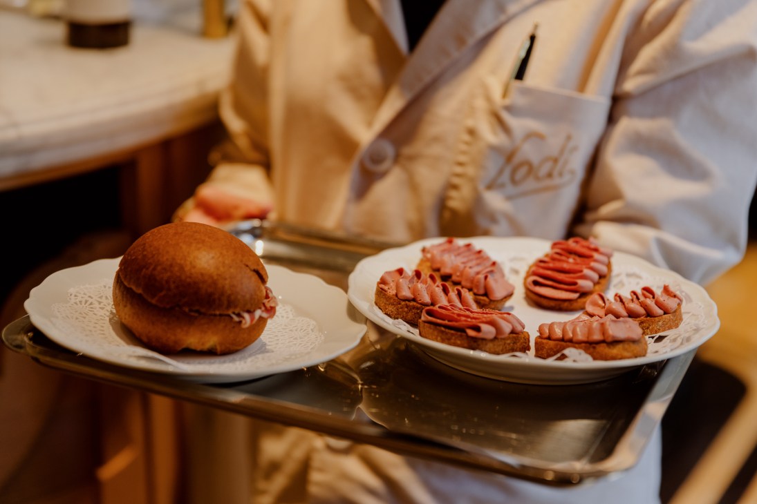 A sandwich and four open-faced sandwiches topped with sliced cured meat on white plates