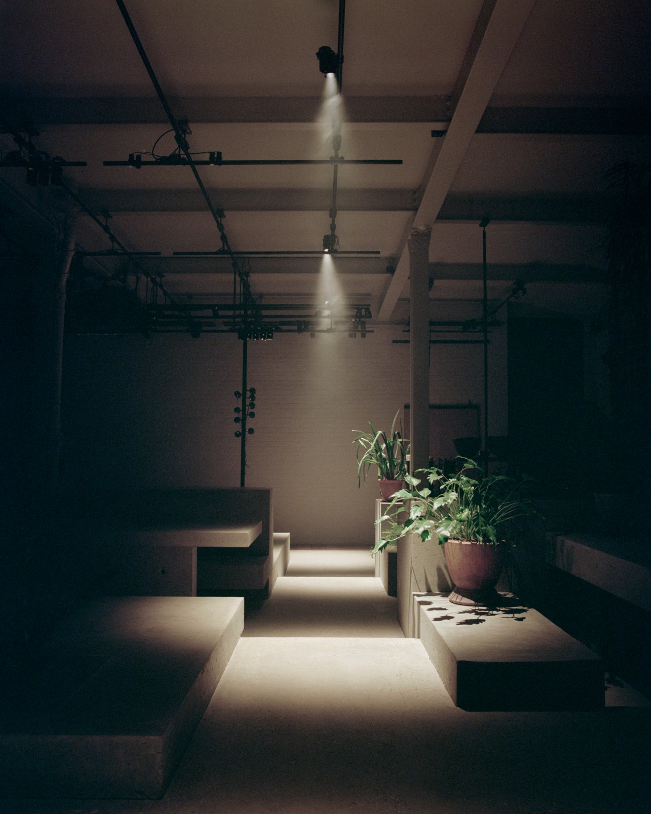 Modern industrial interior with exposed ceiling, dramatic spotlighting, stepped seating and potted plants