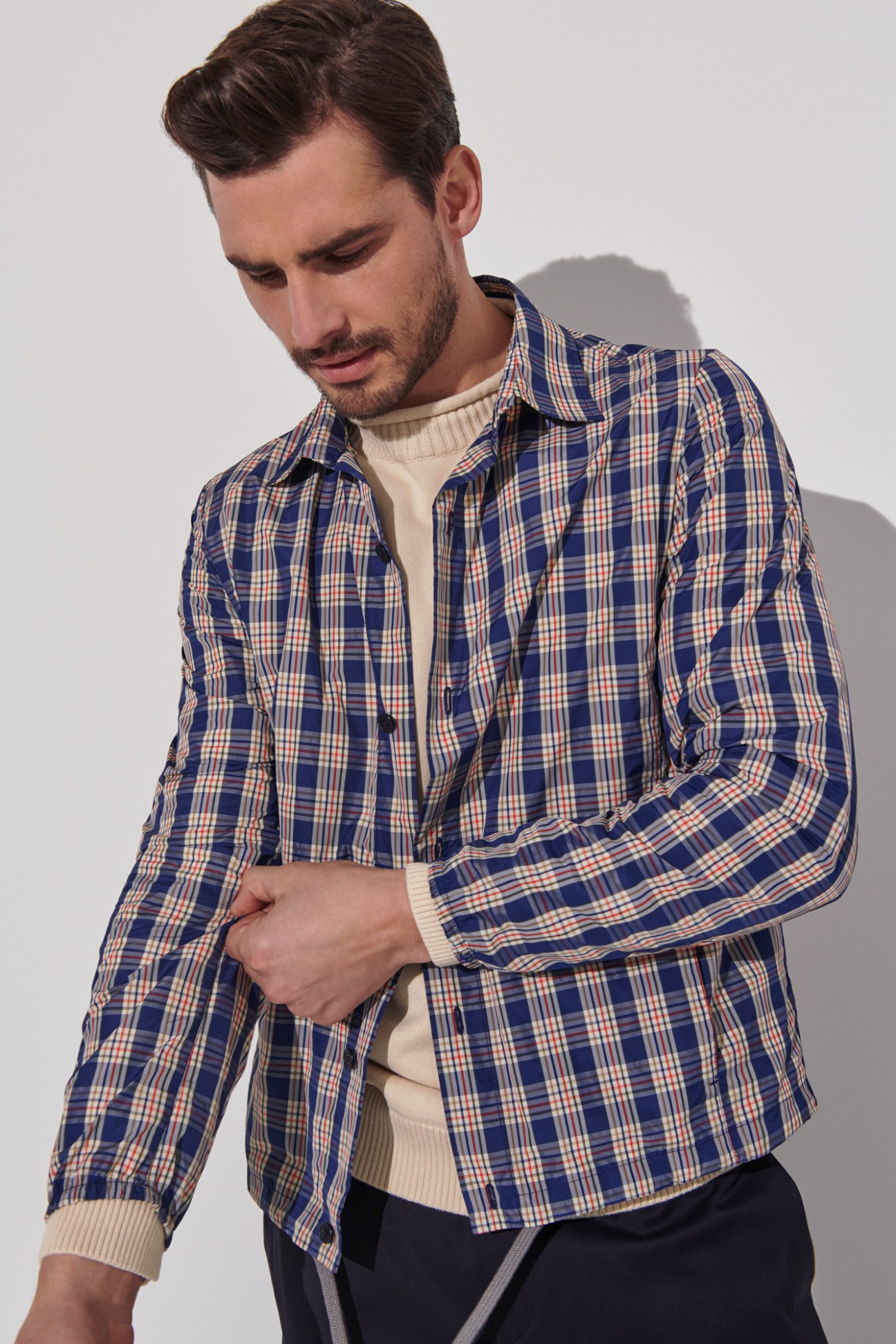 Man wearing blue plaid button-up shirt over cream turtleneck sweater