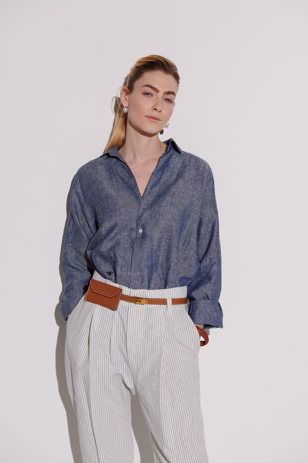 Woman in blue denim shirt and white pinstriped trousers with brown leather belt bag