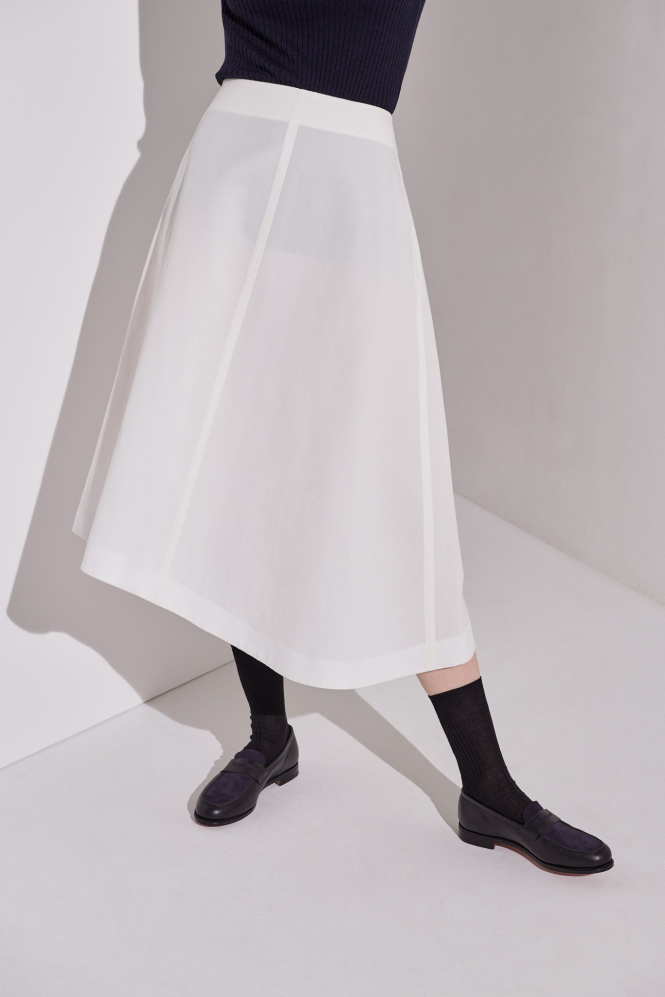 Woman wearing navy ribbed polo shirt, white midi skirt, black knee-high socks and black leather loafers
