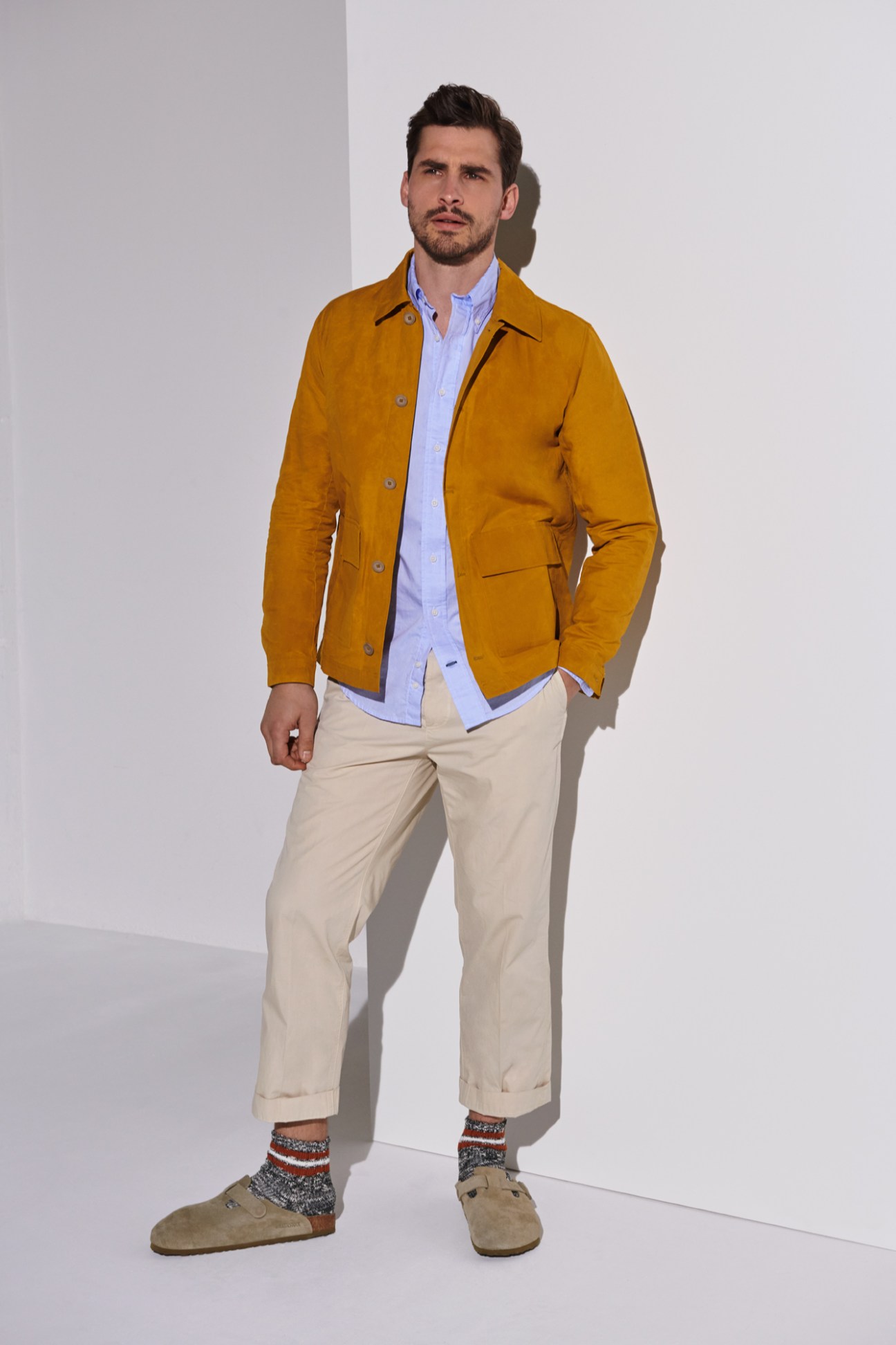 Man wearing mustard yellow jacket by A Kind of Guise over blue shirt with beige trousers and patterned socks