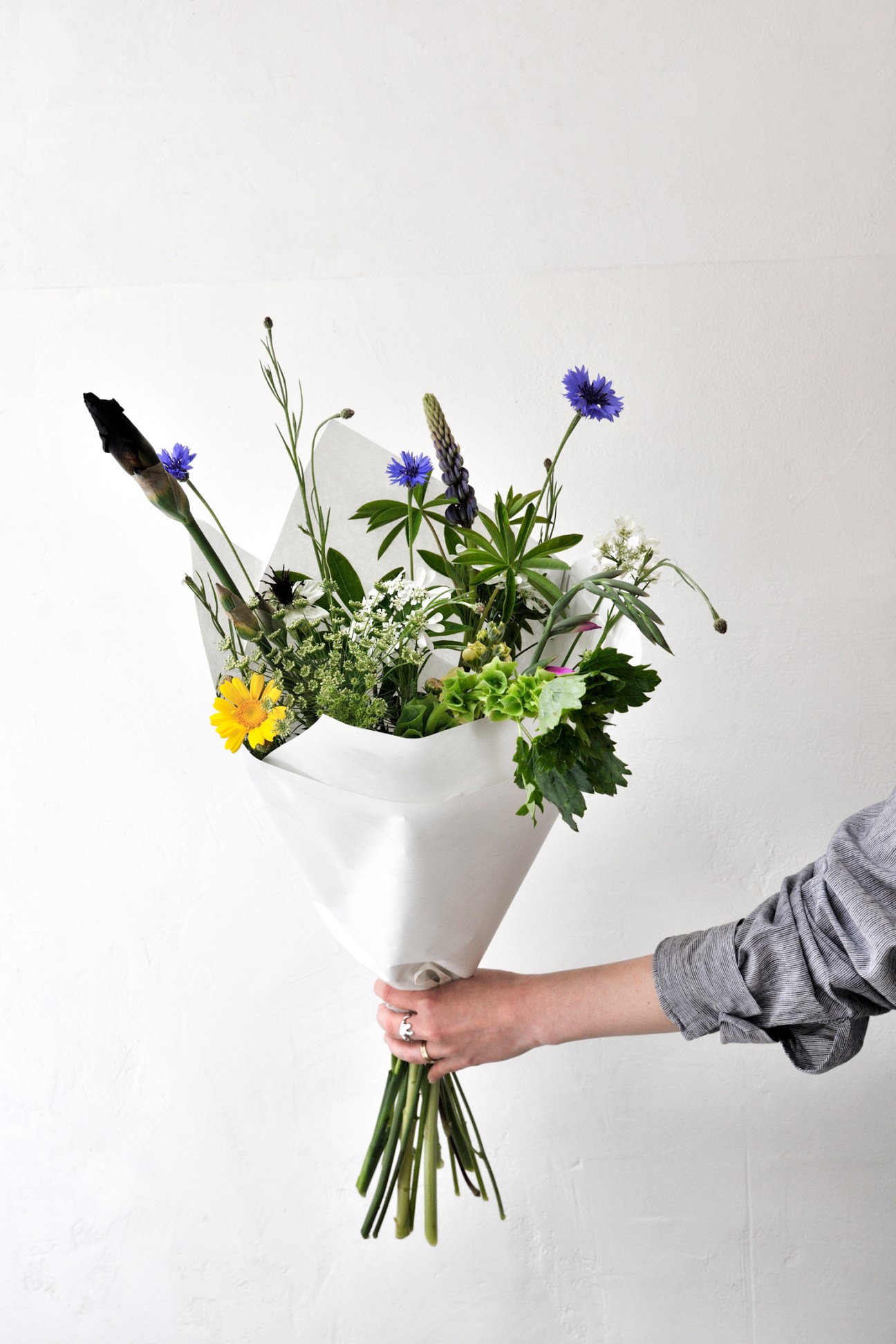 Hand holding a wildflower bouquet wrapped in white paper against neutral background