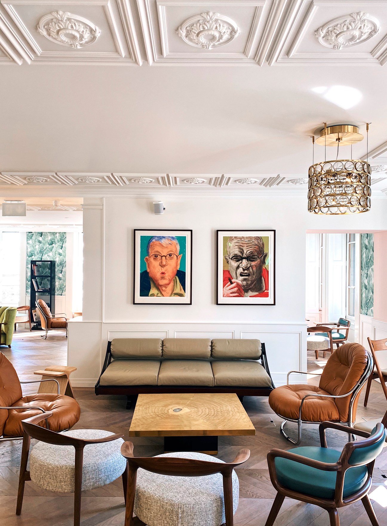 Modern lobby with ornate ceiling, contemporary furniture, crystal chandelier and framed portraits on white walls