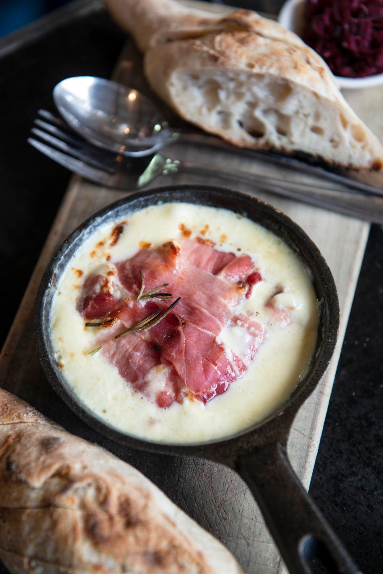 Sliced cured ham arranged on creamy white sauce in a black cast iron pan with bread and herbs
