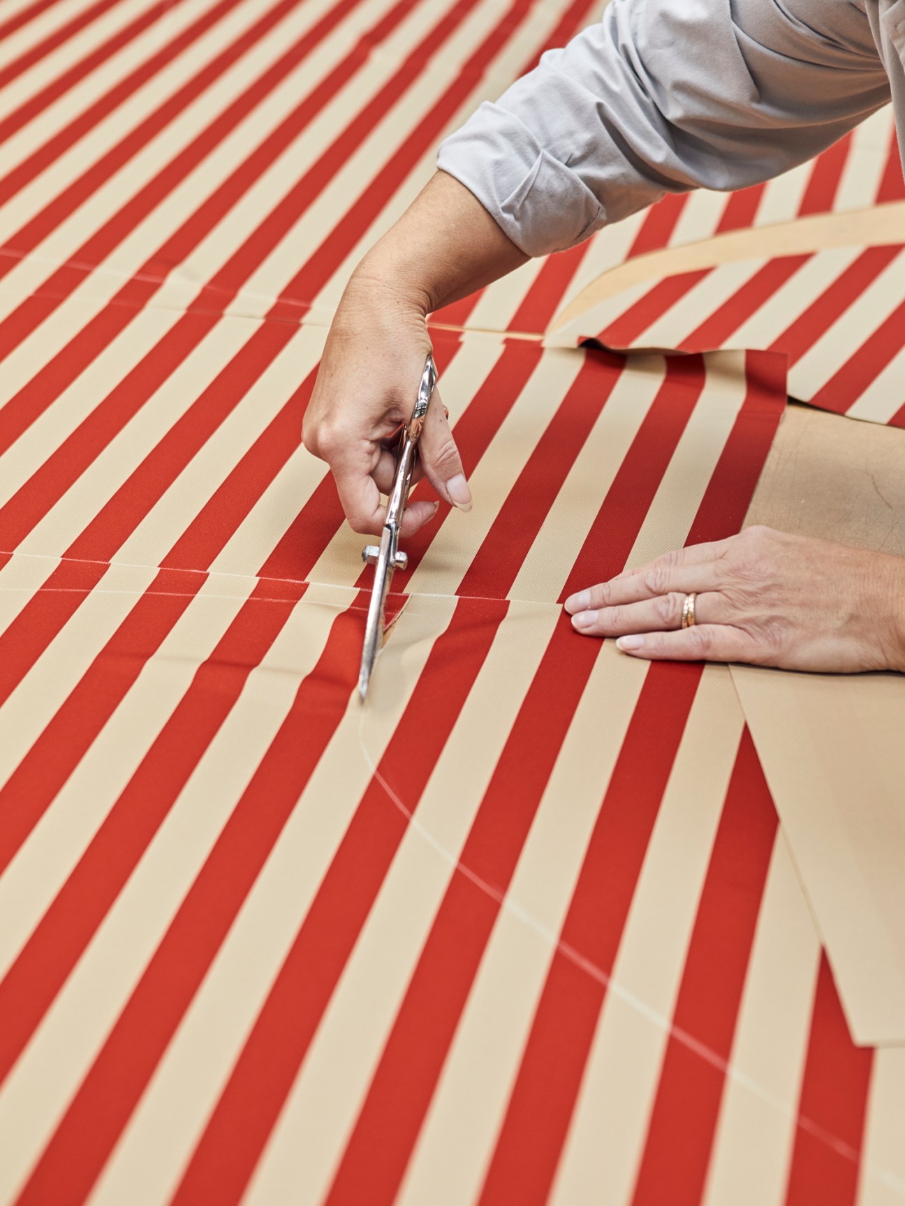Hands using scissors to cut red and white striped fabric on a work surface
