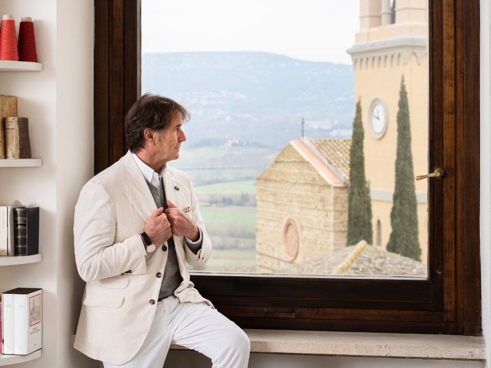 Man in white suit sitting by window overlooking Italian countryside with bell tower and cypress trees