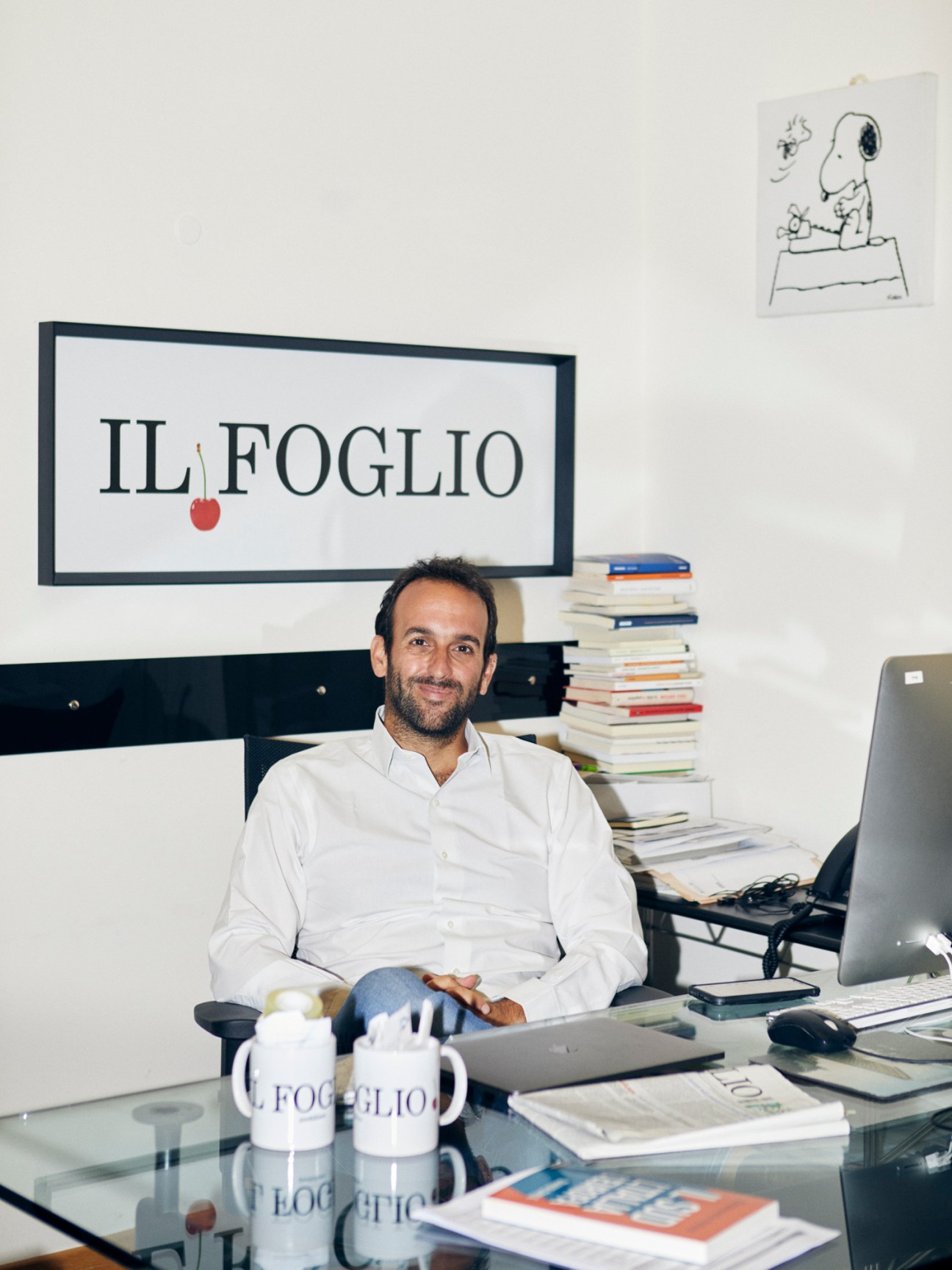 Il Foglio editor Claudio Cerasa sits at his desk in the Rome office surrounded by stacks of books and newspapers.